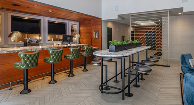 Chic bar area with green bar stools, a long communal table, and stylish lighting at The Clark Apartments in Chicago