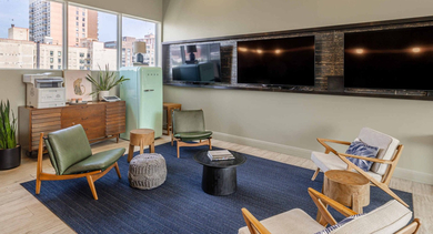 Stylish resident game and TV lounge with modern gray sectional seating, a media wall, and a mint green SMEG refrigerator at The Clark