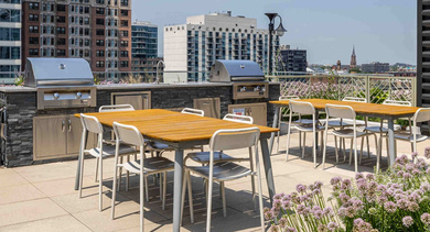 Modern rooftop deck with stainless steel grills, a dining area, and stunning Chicago skyline views at The Clark Apartments
