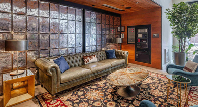 Stylish community lounge with a large green Chesterfield sofa, ornate rug, and modern wall decor at The Clark Apartments in Chicago
