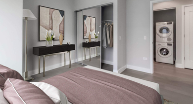Stylish bedroom with a large bed, mirrored closet doors, and convenient in-unit stacked laundry machines at The Clark Apartments in Chicago