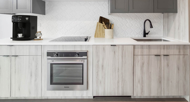 Sleek and modern kitchen with light wood and grey cabinets, integrated appliances, and open shelving at The Clark Apartments in Chicago