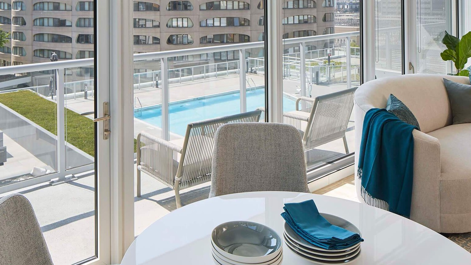 Cozy dining area with a round table and chairs, overlooking a balcony with pool views and city architecture at The Cooper in Chicago