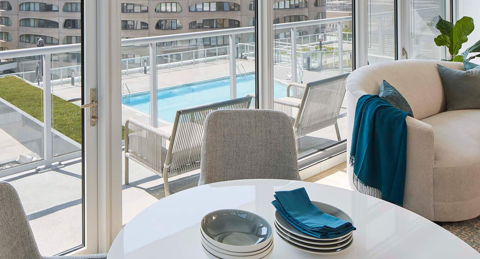 Cozy dining area with a round table and chairs, overlooking a balcony with pool views and city architecture at The Cooper in Chicago