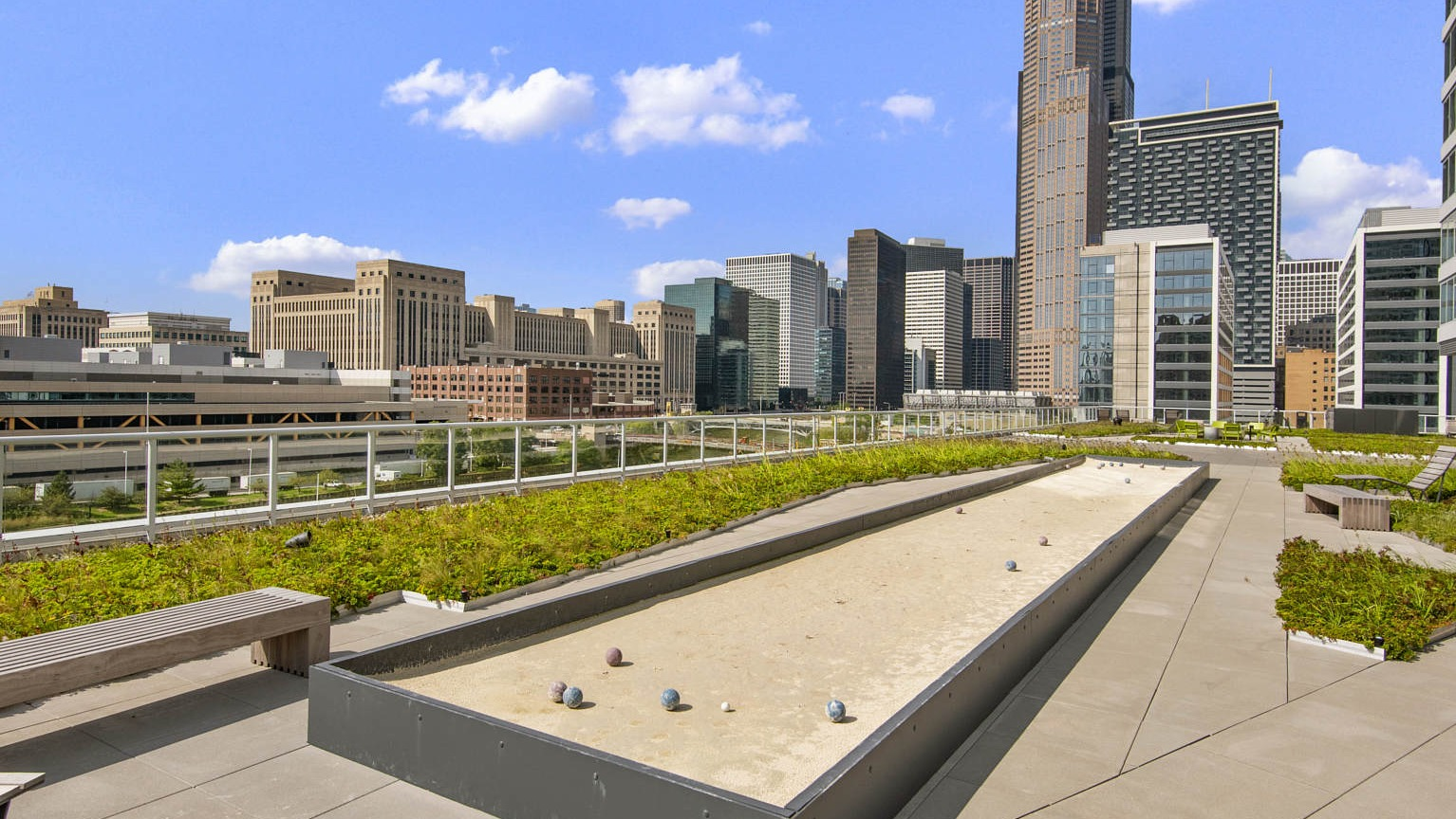 Outdoor bocce ball court on a green terrace with benches, set against a stunning Chicago skyline at The Cooper apartments
