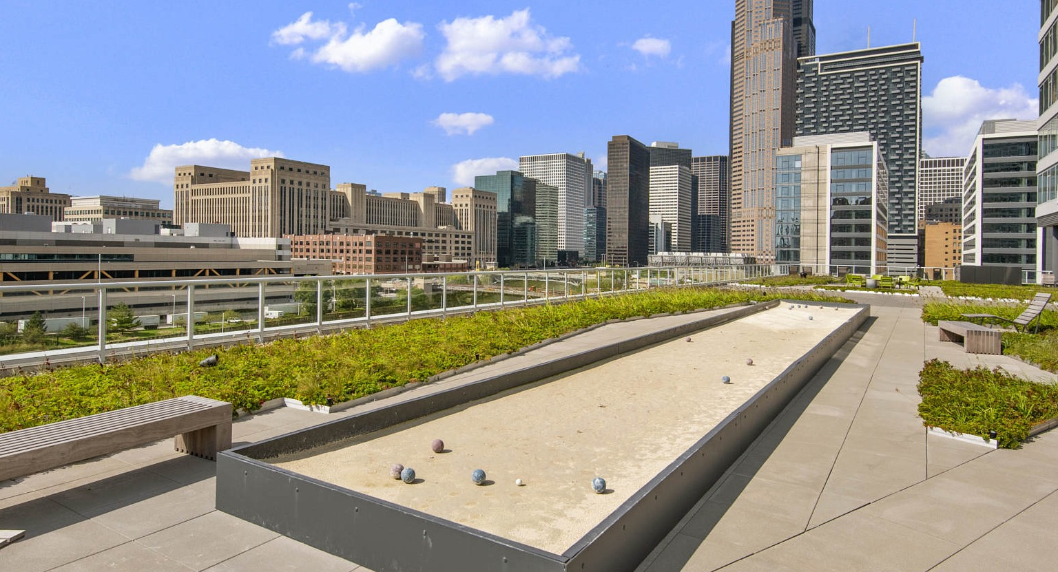 Outdoor bocce ball court on a green terrace with benches, set against a stunning Chicago skyline at The Cooper apartments
