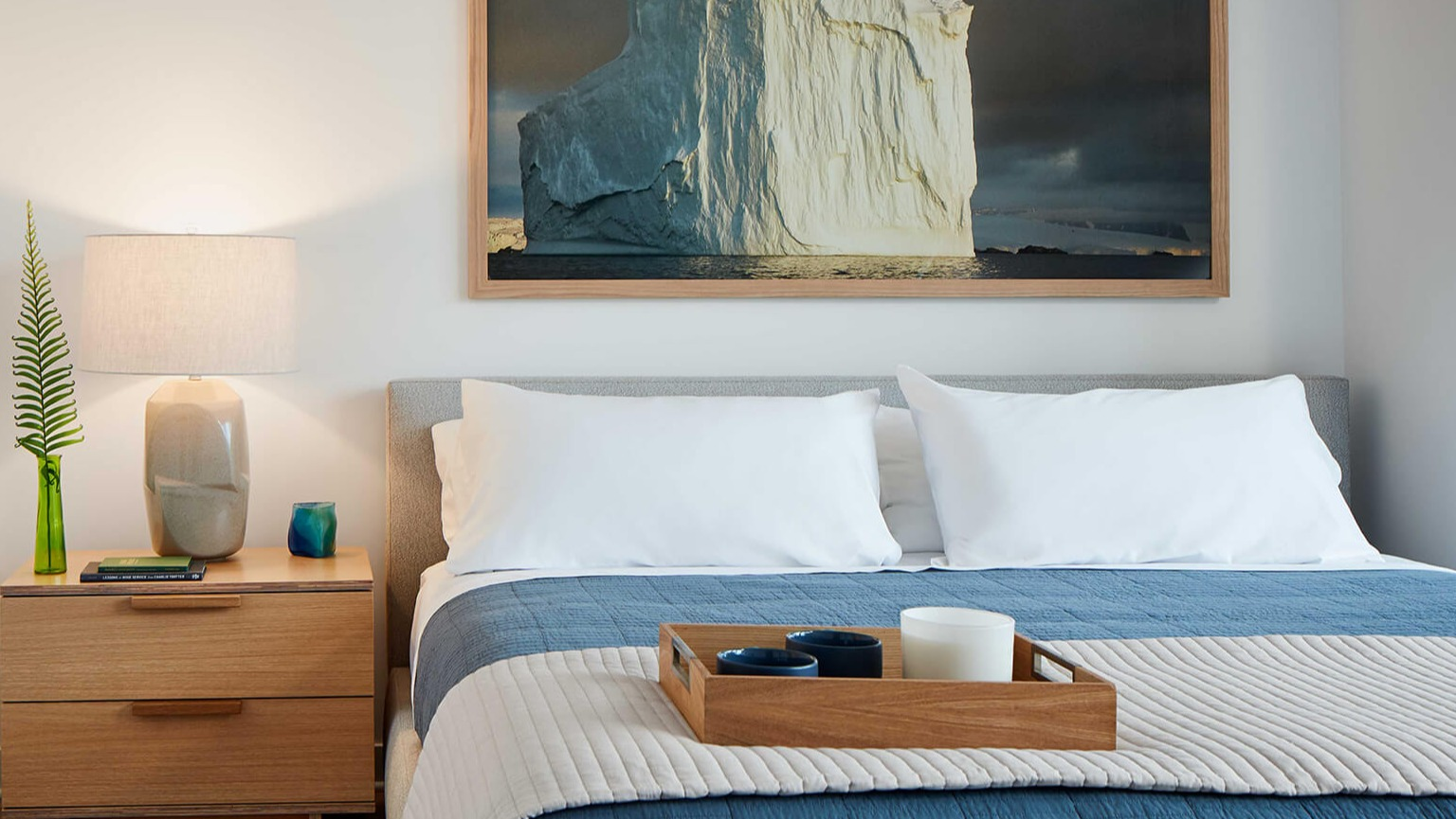 Cozy bedroom with a comfortable bed, warm lighting, wooden nightstand, and an artistic accent piece at The Cooper apartments in Chicago