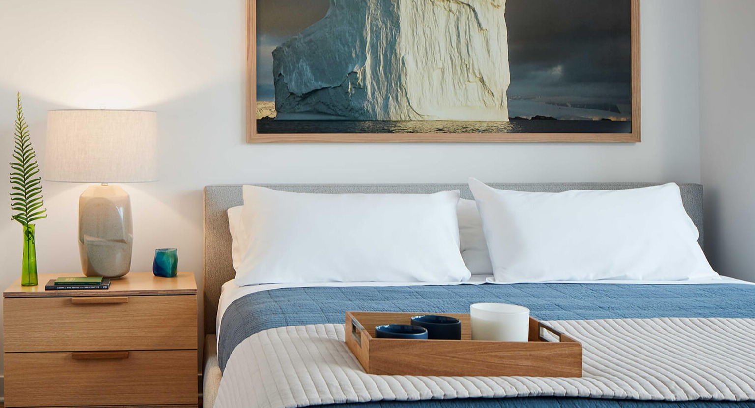 Cozy bedroom with a comfortable bed, warm lighting, wooden nightstand, and an artistic accent piece at The Cooper apartments in Chicago