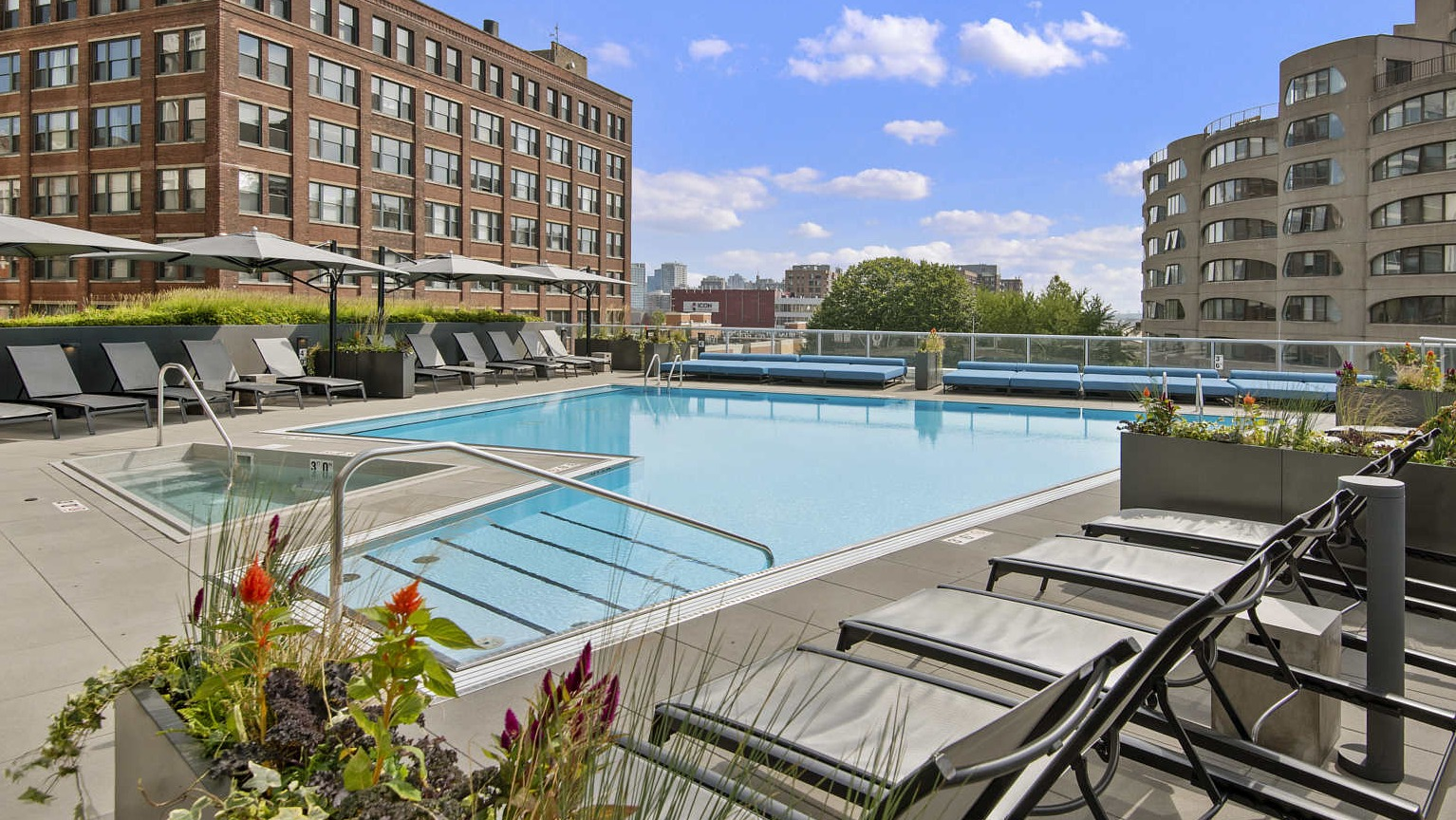 Expansive rooftop deck with a large swimming pool, numerous lounge chairs, and city buildings in the background at The Cooper in Chicago