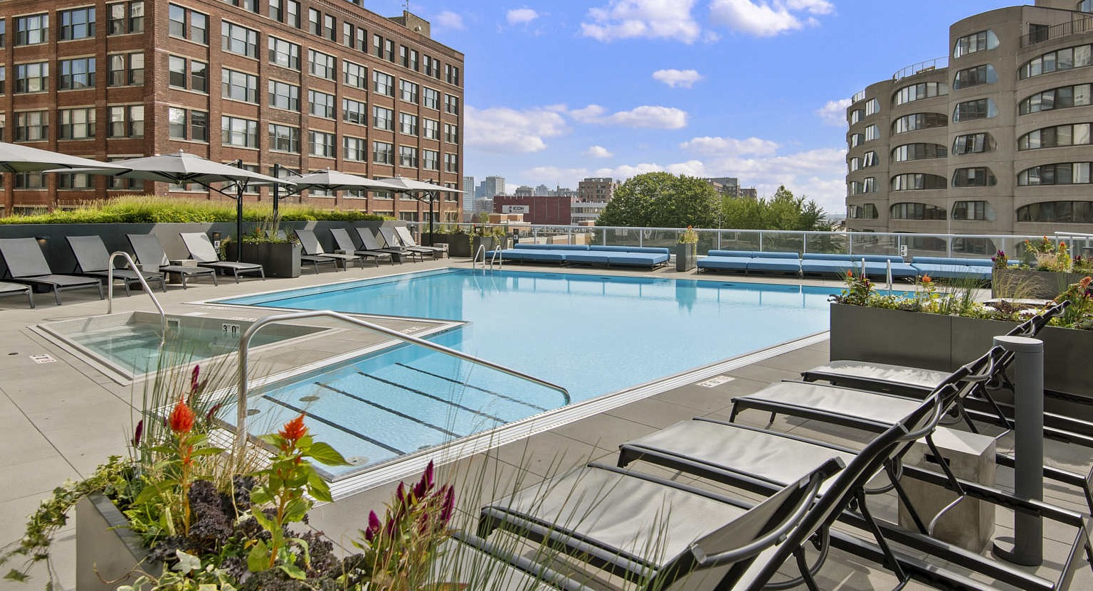 Expansive rooftop deck with a large swimming pool, numerous lounge chairs, and city buildings in the background at The Cooper in Chicago