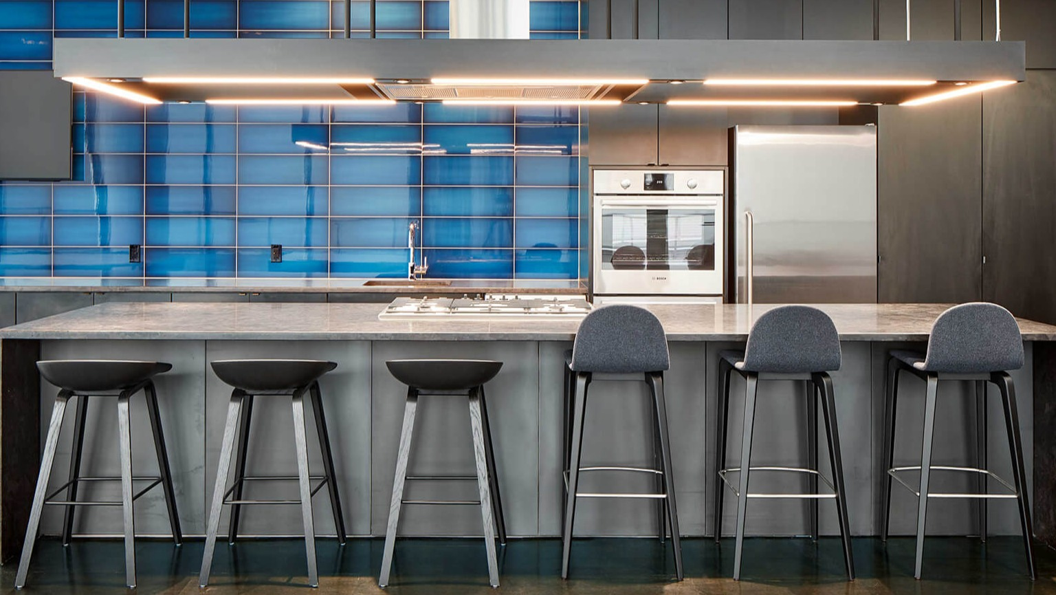 Modern gourmet community kitchen with blue tile backsplash, large island with bar stools, and stainless steel appliances at The Cooper in Chicago