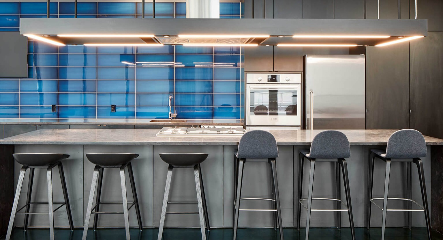 Modern gourmet community kitchen with blue tile backsplash, large island with bar stools, and stainless steel appliances at The Cooper in Chicago