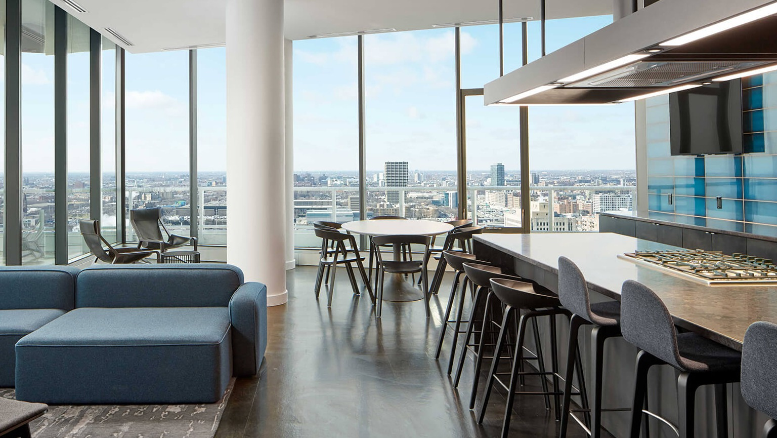 Luxurious high-rise lounge and kitchen with panoramic city views, modern island seating, and comfortable blue sofas at The Cooper in Chicago