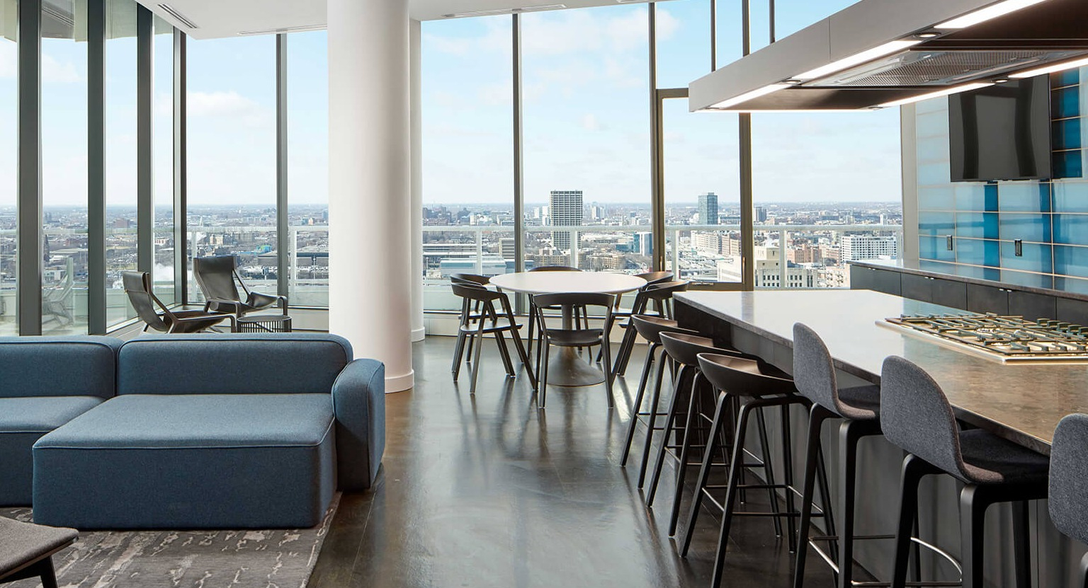 Luxurious high-rise lounge and kitchen with panoramic city views, modern island seating, and comfortable blue sofas at The Cooper in Chicago