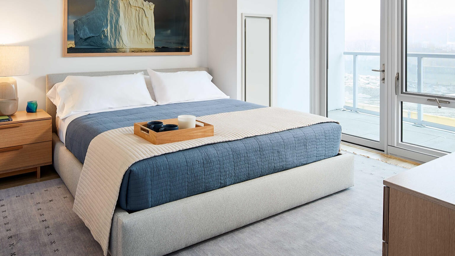 Cozy master bedroom featuring a large bed, modern nightstands, and expansive windows with city views at The Cooper apartments in Chicago