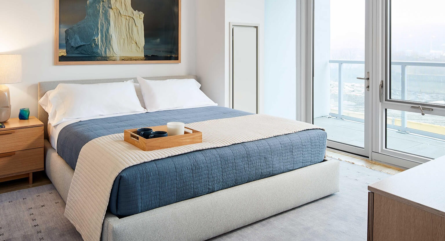 Cozy master bedroom featuring a large bed, modern nightstands, and expansive windows with city views at The Cooper apartments in Chicago