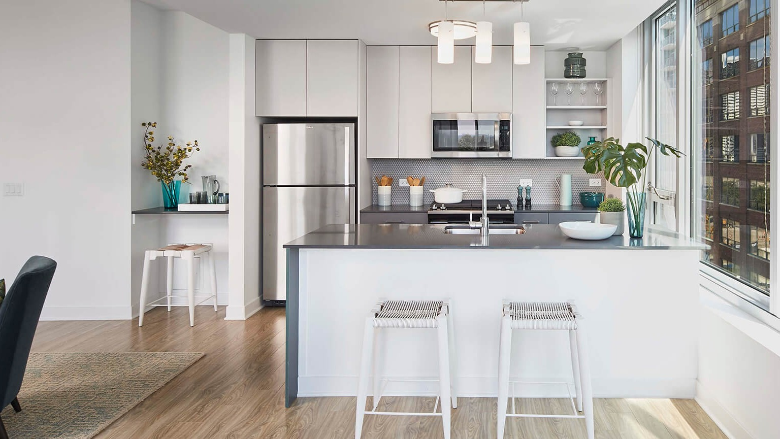 Sleek modern apartment kitchen with light cabinetry, stainless steel appliances, island with bar stools, and large windows at The Cooper in Chicago