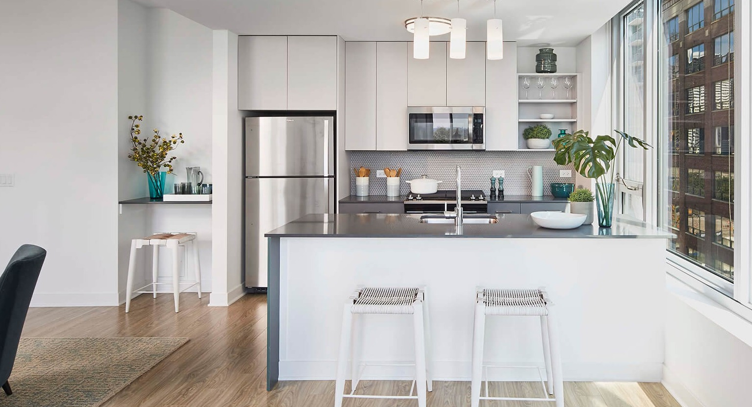 Sleek modern apartment kitchen with light cabinetry, stainless steel appliances, island with bar stools, and large windows at The Cooper in Chicago