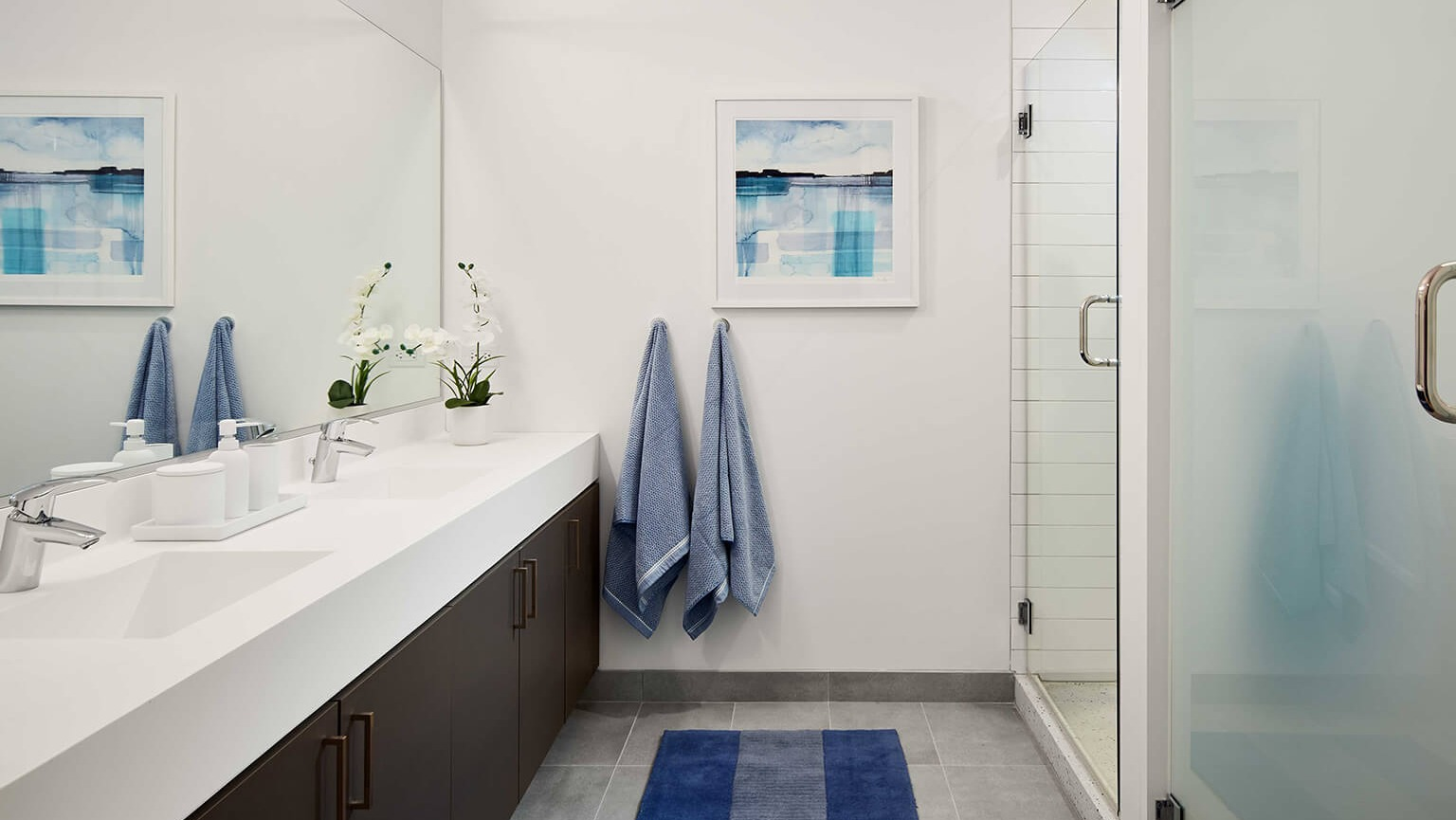 Modern bathroom with a spacious double vanity, large mirror, walk-in shower, and contemporary blue accents at The Cooper in Chicago