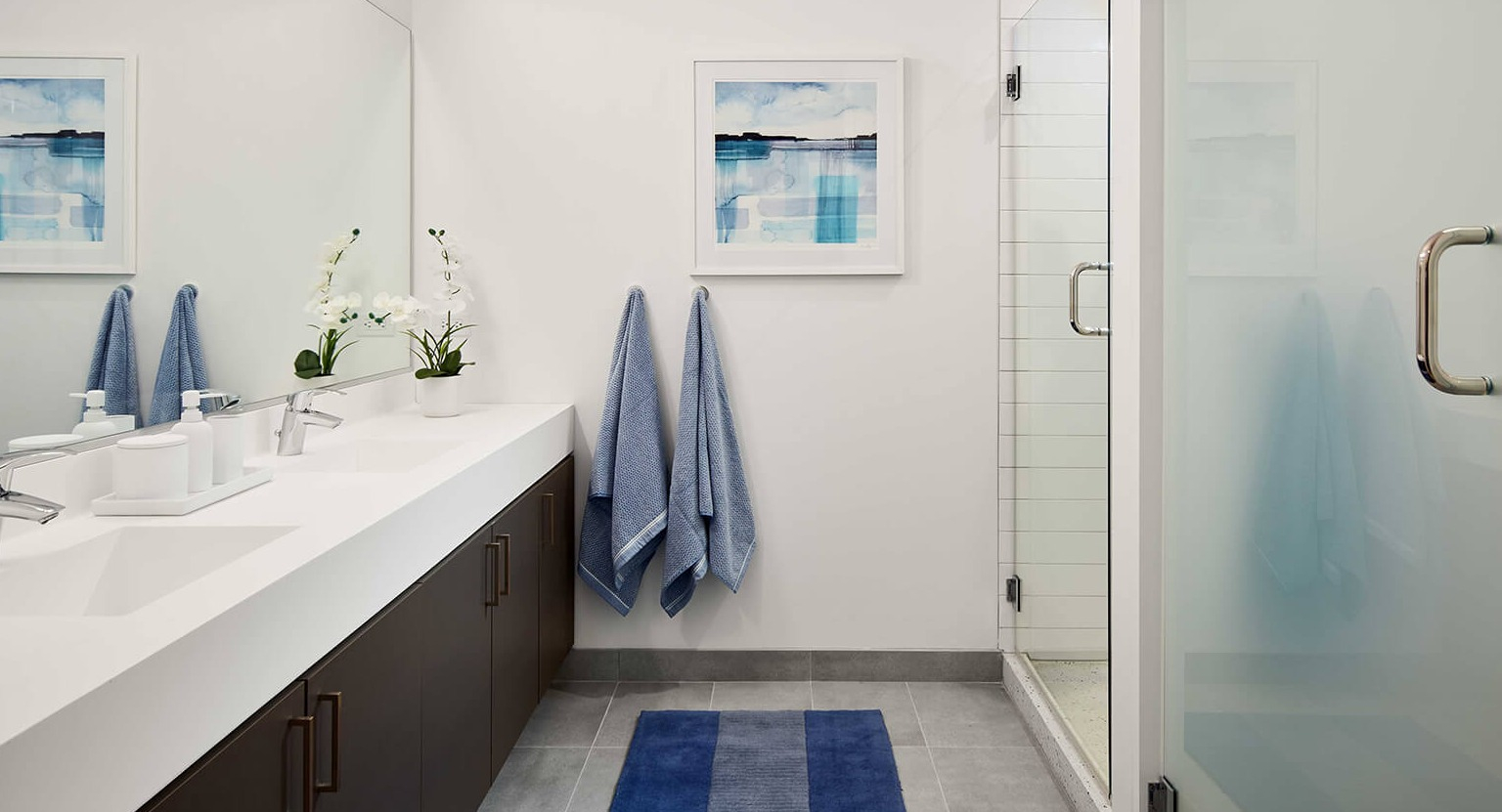 Modern bathroom with a spacious double vanity, large mirror, walk-in shower, and contemporary blue accents at The Cooper in Chicago