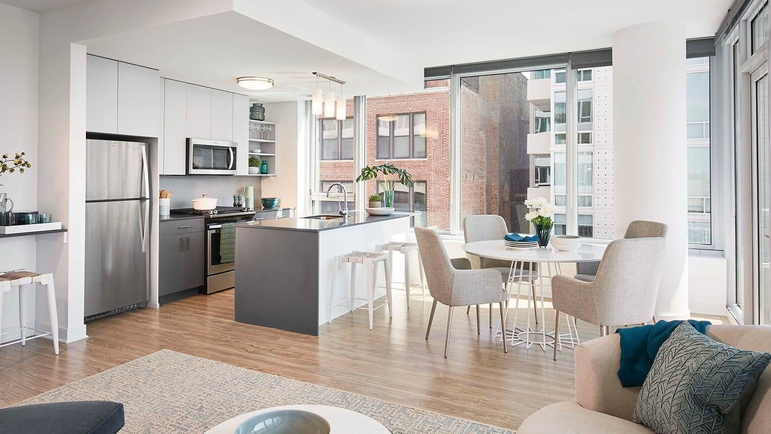 Bright open-concept apartment with a modern kitchen, island seating, dining area, and large windows at The Cooper in Chicago