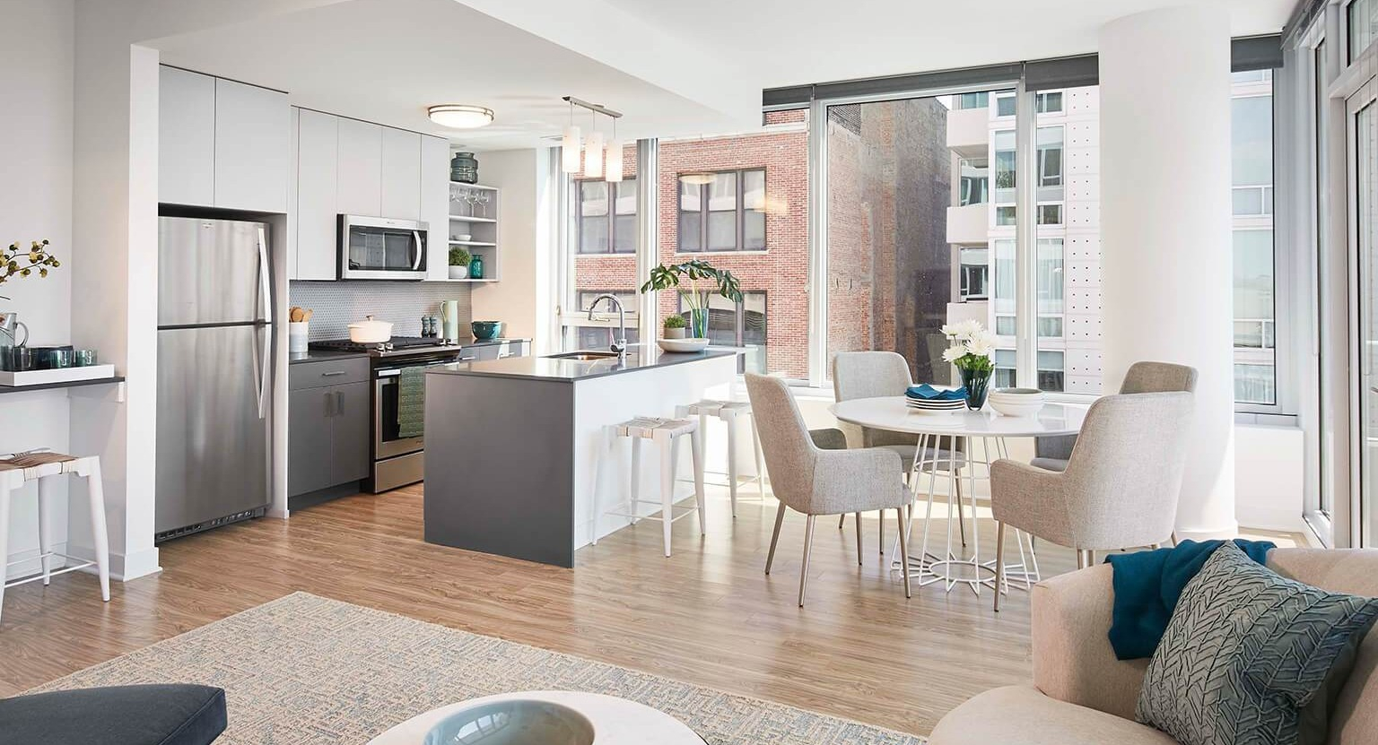 Bright open-concept apartment with a modern kitchen, island seating, dining area, and large windows at The Cooper in Chicago