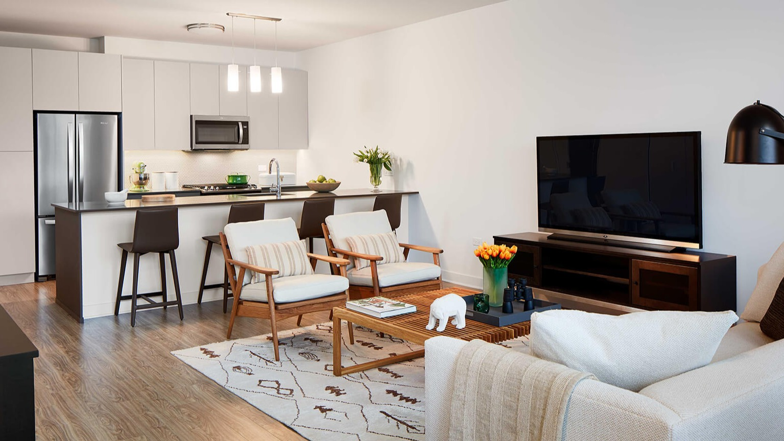 Modern open-concept living room and kitchen with sleek appliances, island seating, and comfortable furnishings at The Cooper in Chicago