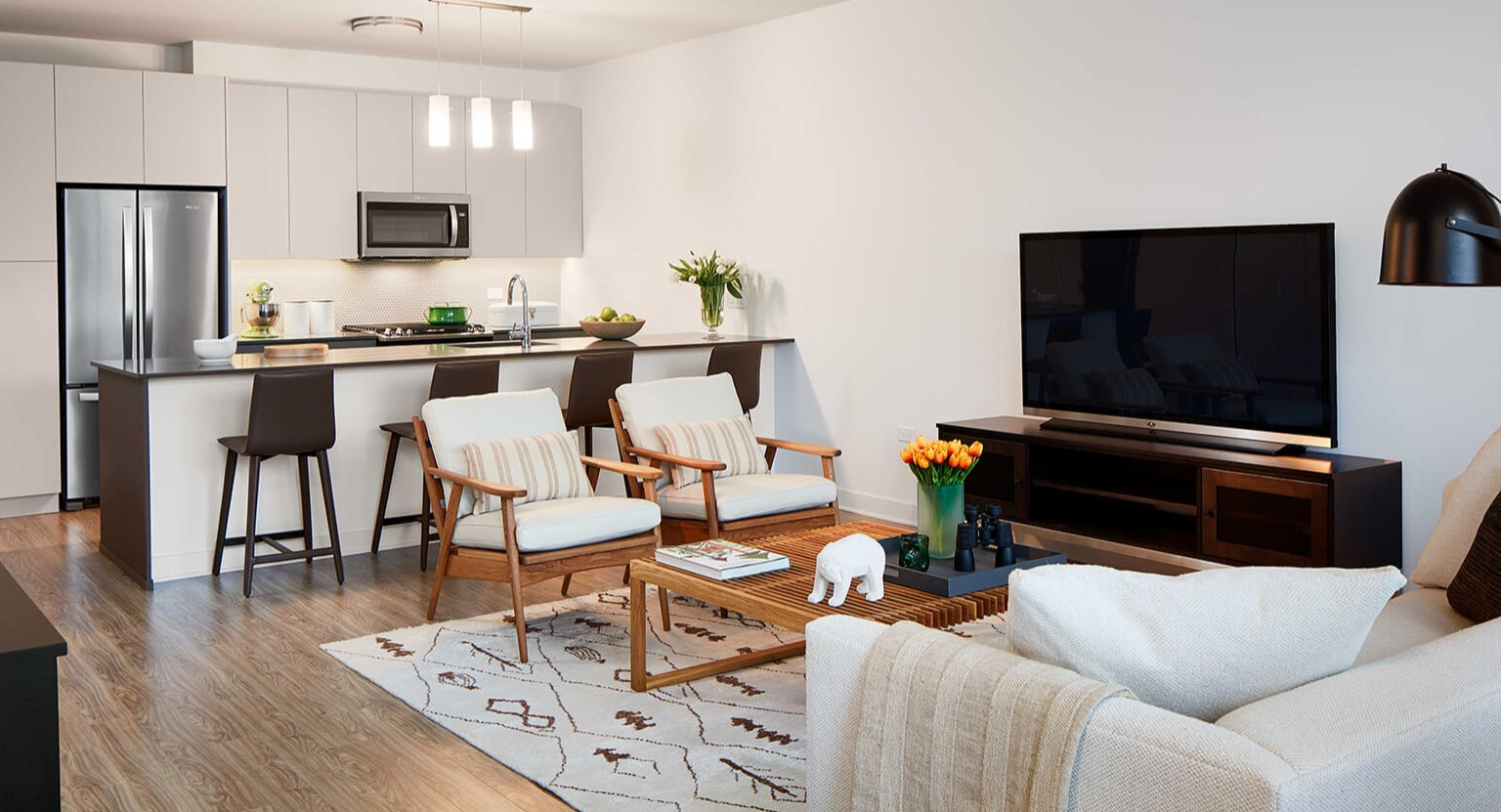 Modern open-concept living room and kitchen with sleek appliances, island seating, and comfortable furnishings at The Cooper in Chicago