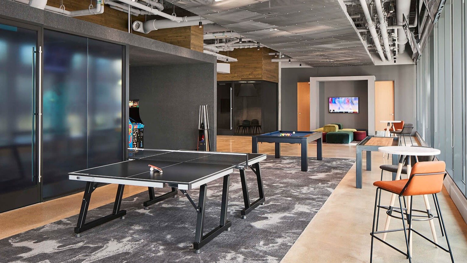 Modern resident game room with ping pong and pool tables, lounge seating, and large windows at The Cooper apartments in Chicago