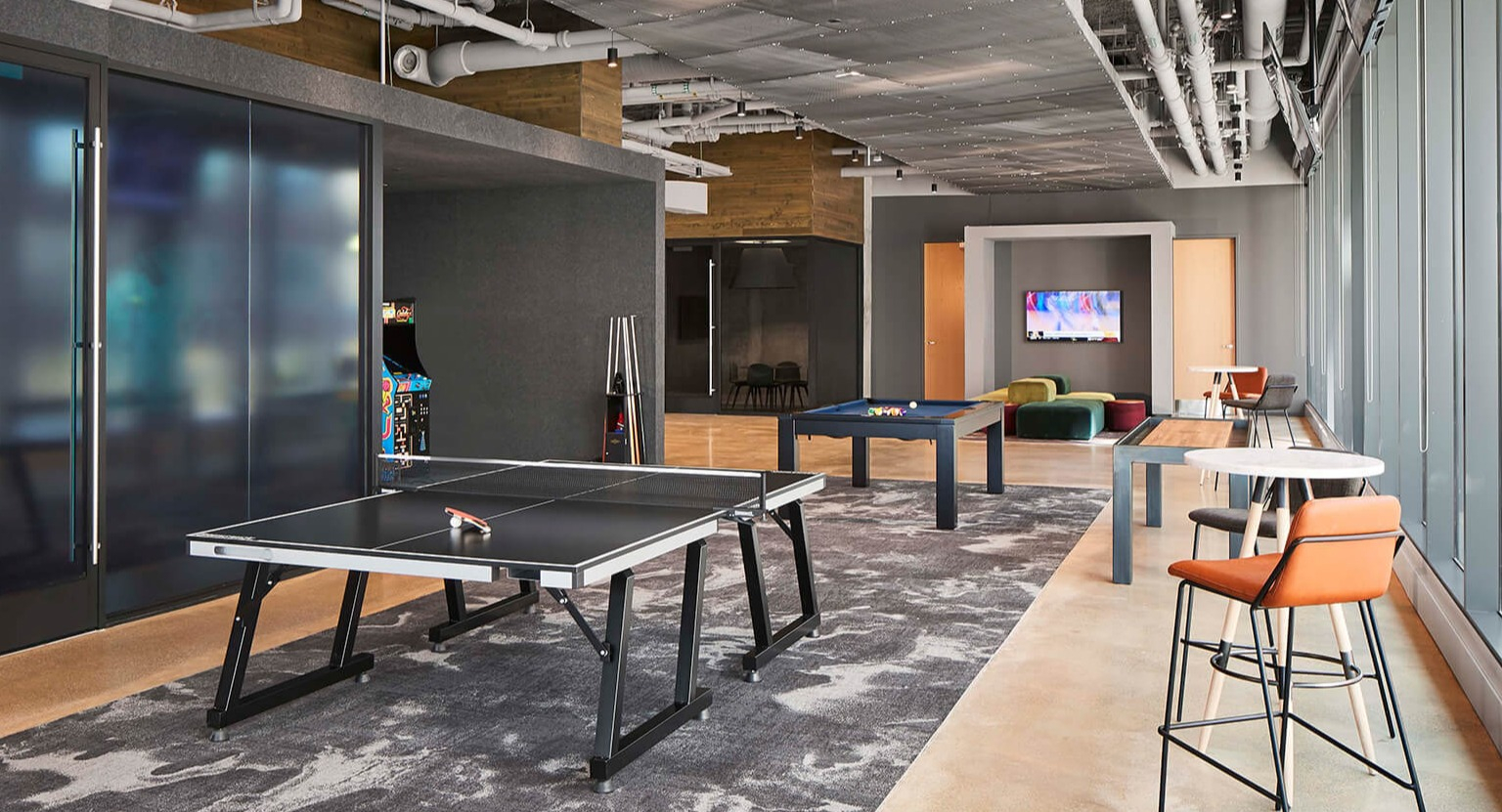 Modern resident game room with ping pong and pool tables, lounge seating, and large windows at The Cooper apartments in Chicago