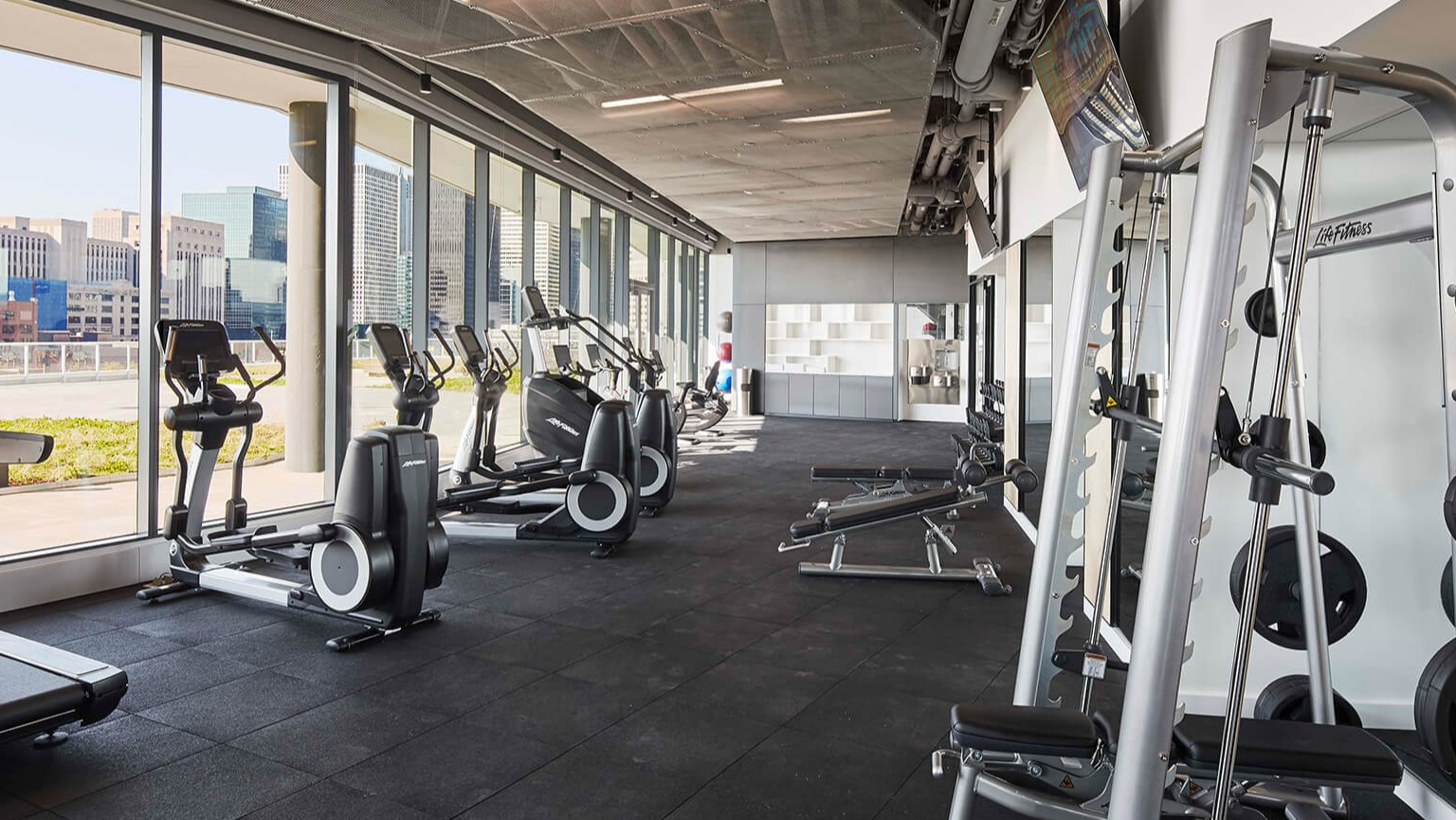 State-of-the-art gym with treadmills, ellipticals, weight machines, and large windows offering city views at The Cooper in Chicago