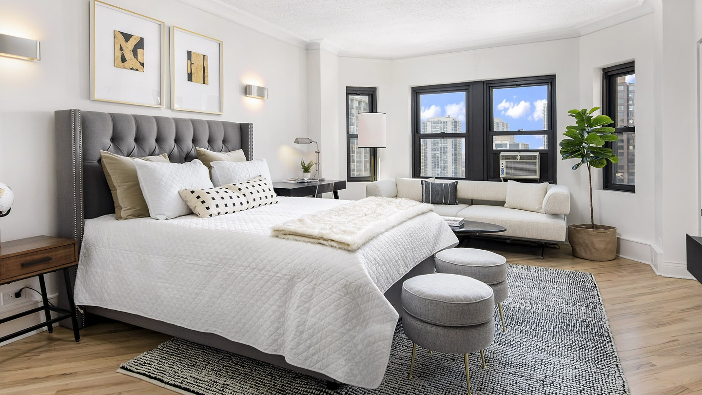Spacious bedroom with a luxurious bed, decorative accents, and a comfortable lounge area by the windows at The Deco North Lake Shore in Chicago