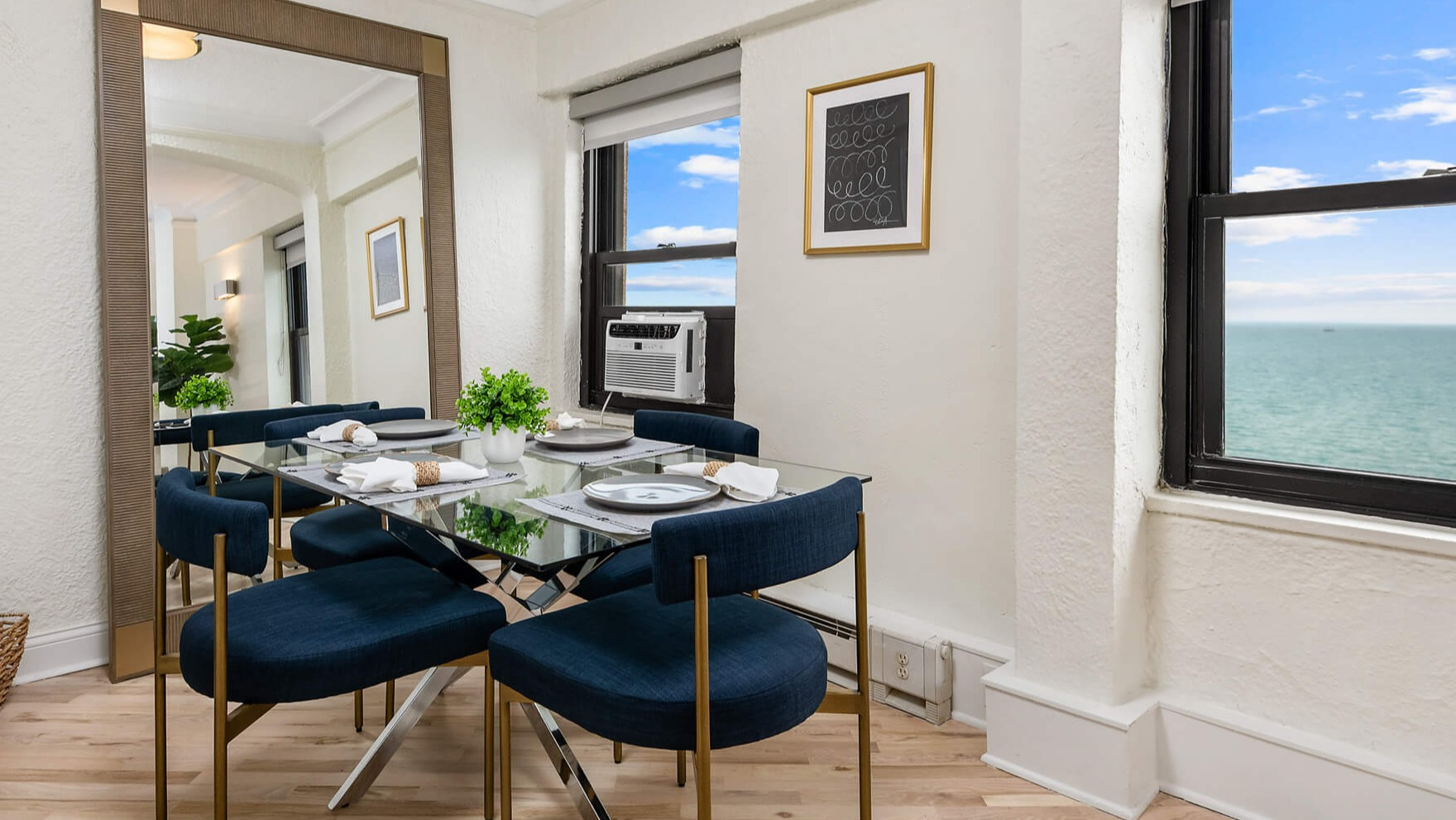 Elegant dining area with a glass table, blue chairs, and stunning lake views from large windows at The Deco North Lake Shore in Chicago