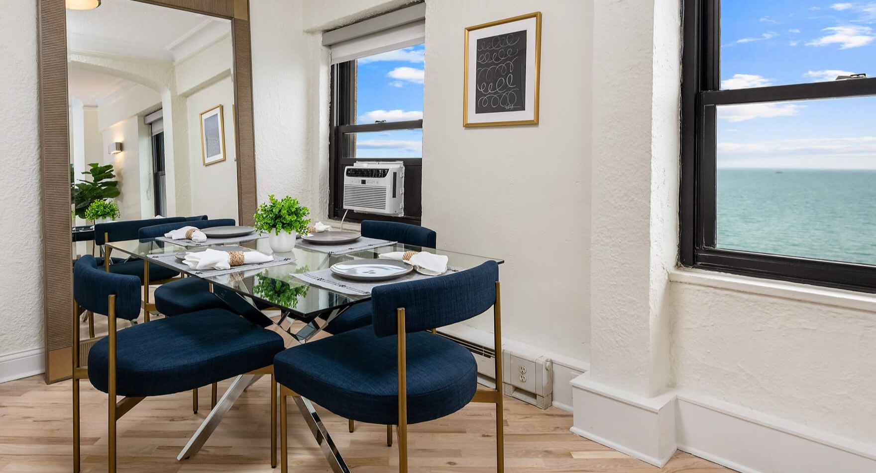 Elegant dining area with a glass table, blue chairs, and stunning lake views from large windows at The Deco North Lake Shore in Chicago