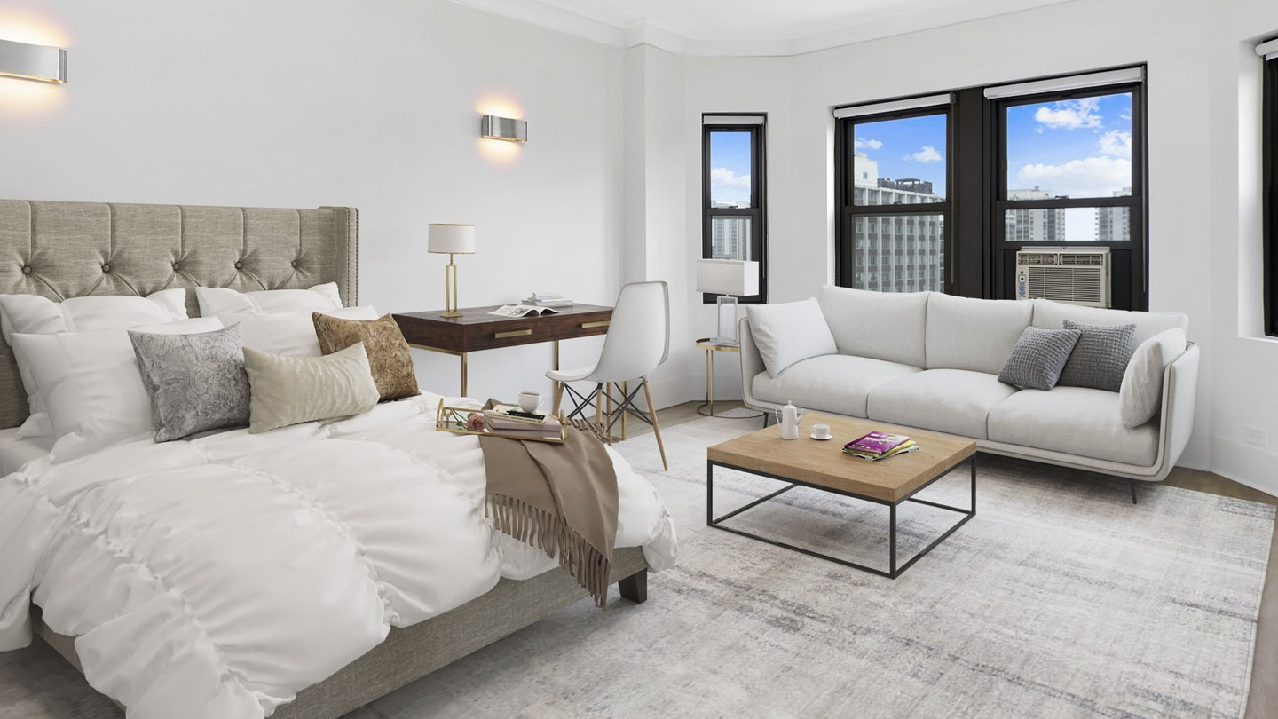 Spacious studio bedroom featuring a large bed, stylish desk, and a comfortable lounge sofa by the windows at The Deco North Lake Shore in Chicago