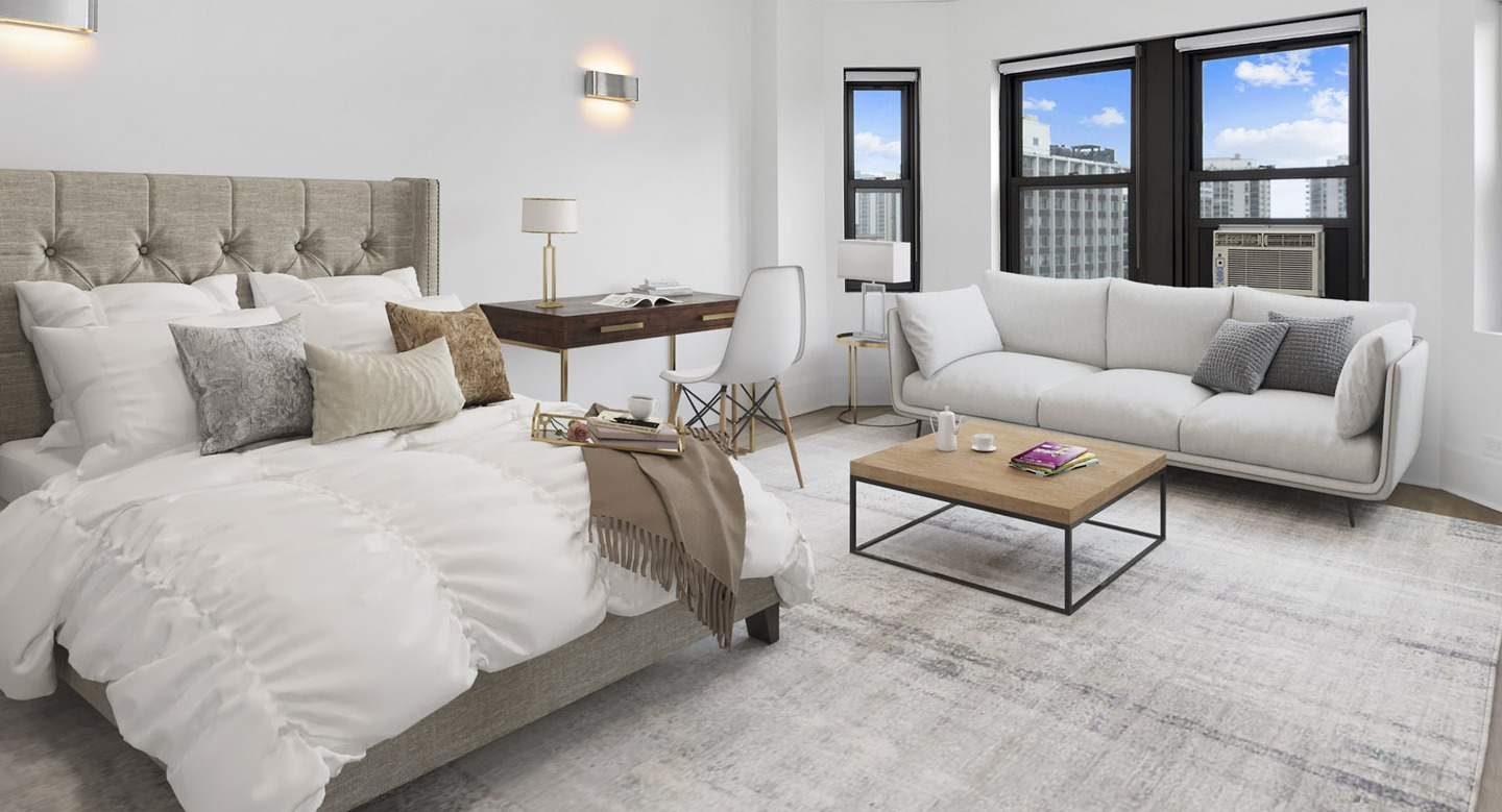 Spacious studio bedroom featuring a large bed, stylish desk, and a comfortable lounge sofa by the windows at The Deco North Lake Shore in Chicago