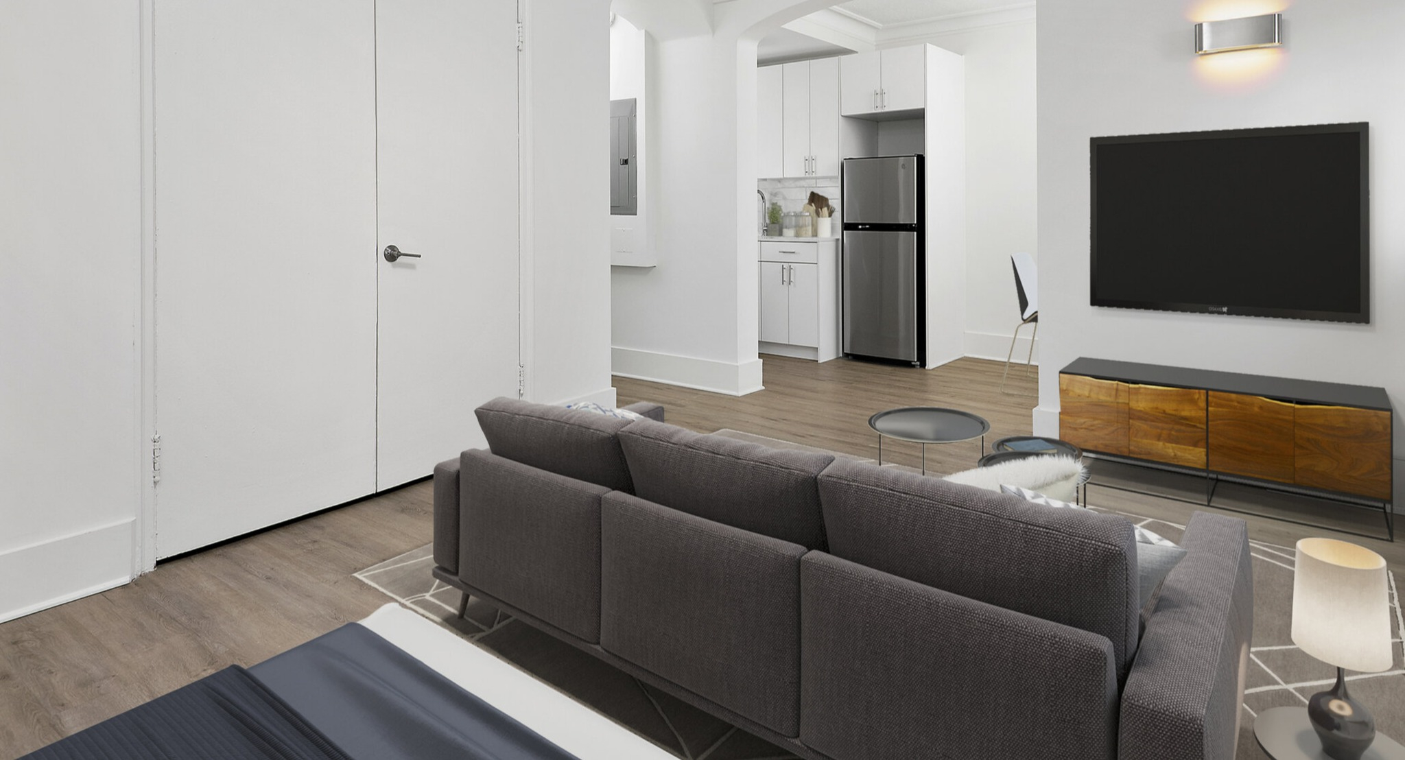 Compact studio living area featuring a comfortable sofa, modern TV unit, and an open entryway to the kitchenette at The Deco North Lake Shore in Chicago