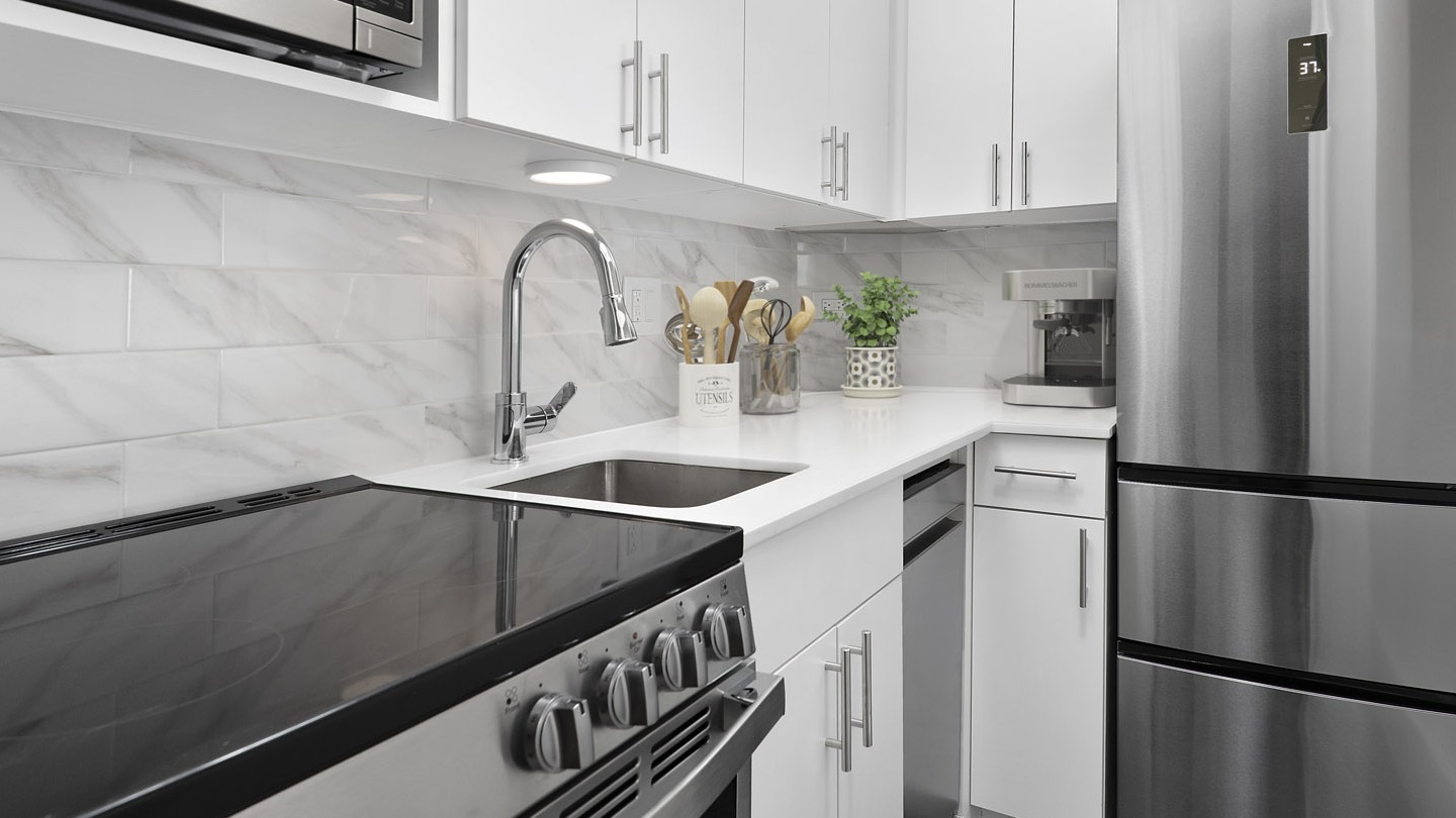 Recently updated kitchen with white cabinetry, stainless steel appliances, marble-patterned backsplash, and a modern sink at The Deco North Lake Shore in Chicago
