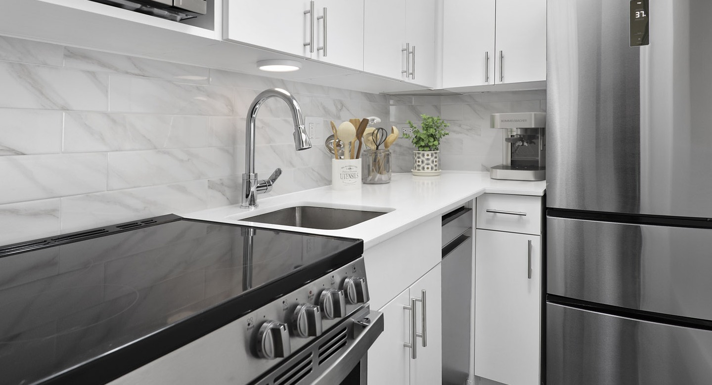 Recently updated kitchen with white cabinetry, stainless steel appliances, marble-patterned backsplash, and a modern sink at The Deco North Lake Shore in Chicago