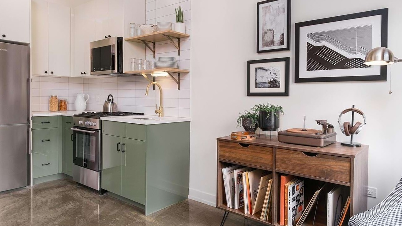 Stylish apartment with a modern kitchen featuring green cabinets, open shelving, and a cozy living area at The Duncan in Chicago