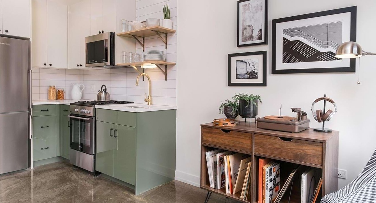 Stylish apartment with a modern kitchen featuring green cabinets, open shelving, and a cozy living area at The Duncan in Chicago