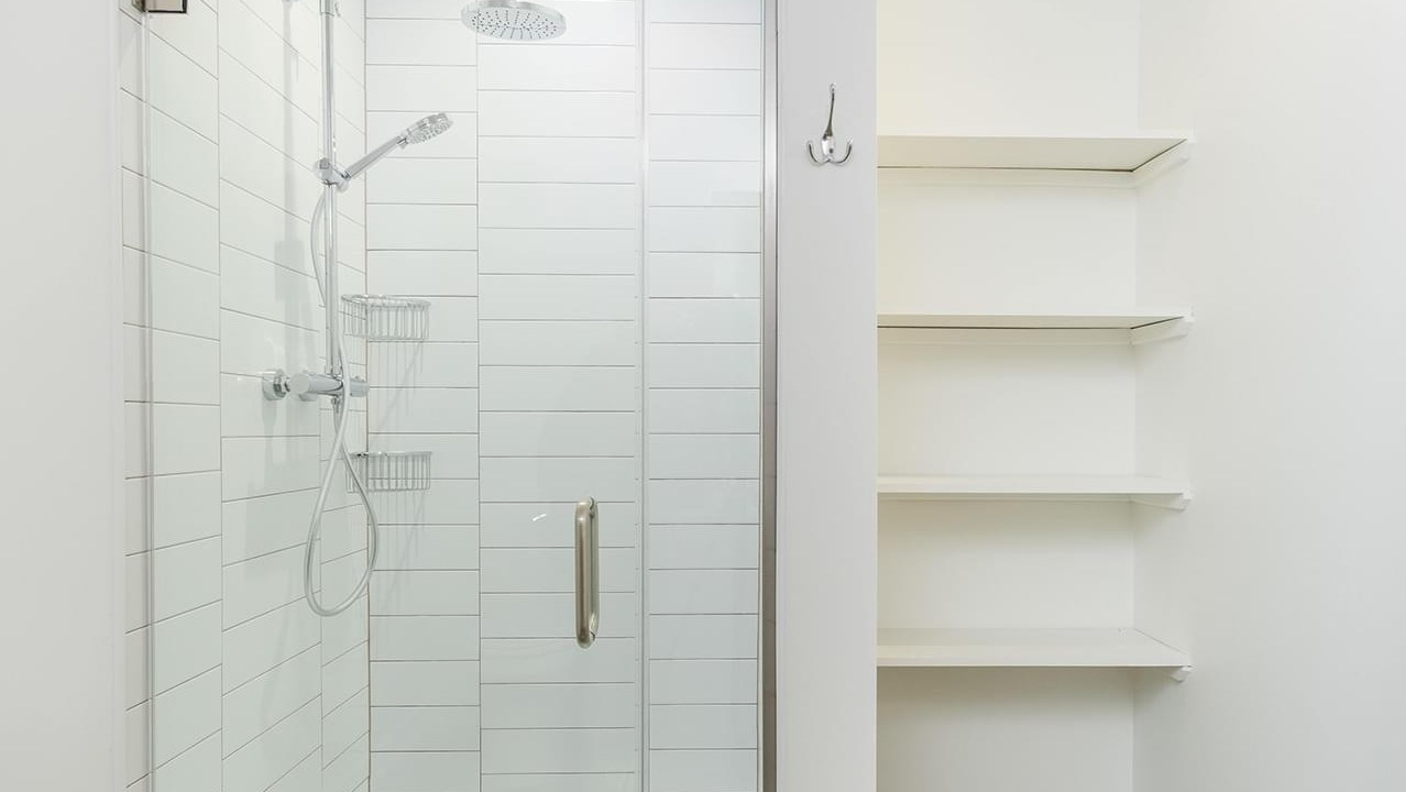 Modern bathroom with a spacious walk-in shower featuring subway tiles and convenient shelving at The Duncan apartments in Chicago