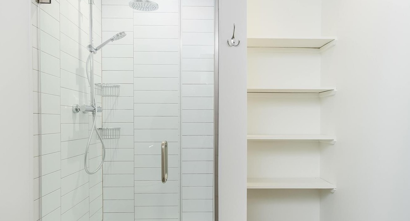 Modern bathroom with a spacious walk-in shower featuring subway tiles and convenient shelving at The Duncan apartments in Chicago