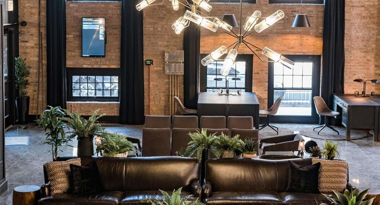 Grand lobby lounge with high ceilings, exposed brick, plush leather sofas, and modern chandeliers at The Duncan apartments in Chicago