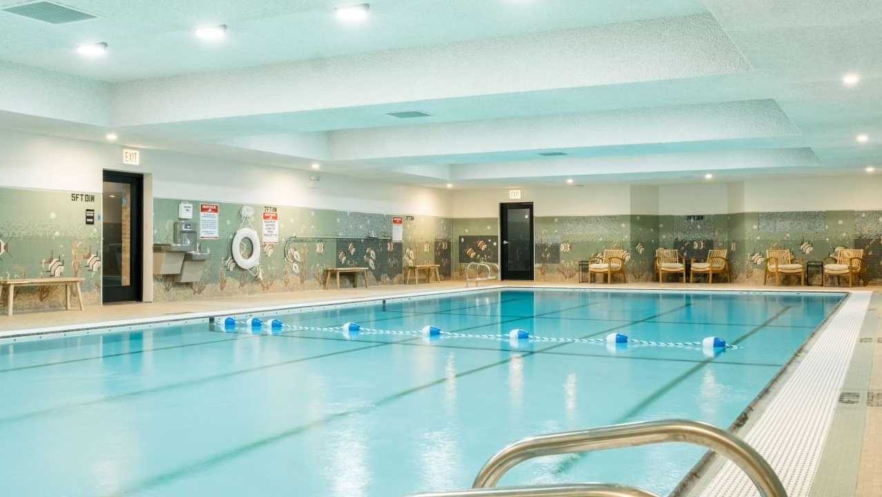 Spacious indoor swimming pool with decorative mosaic tiling, relaxation seating, and bright overhead lighting at The Duncan apartments in Chicago