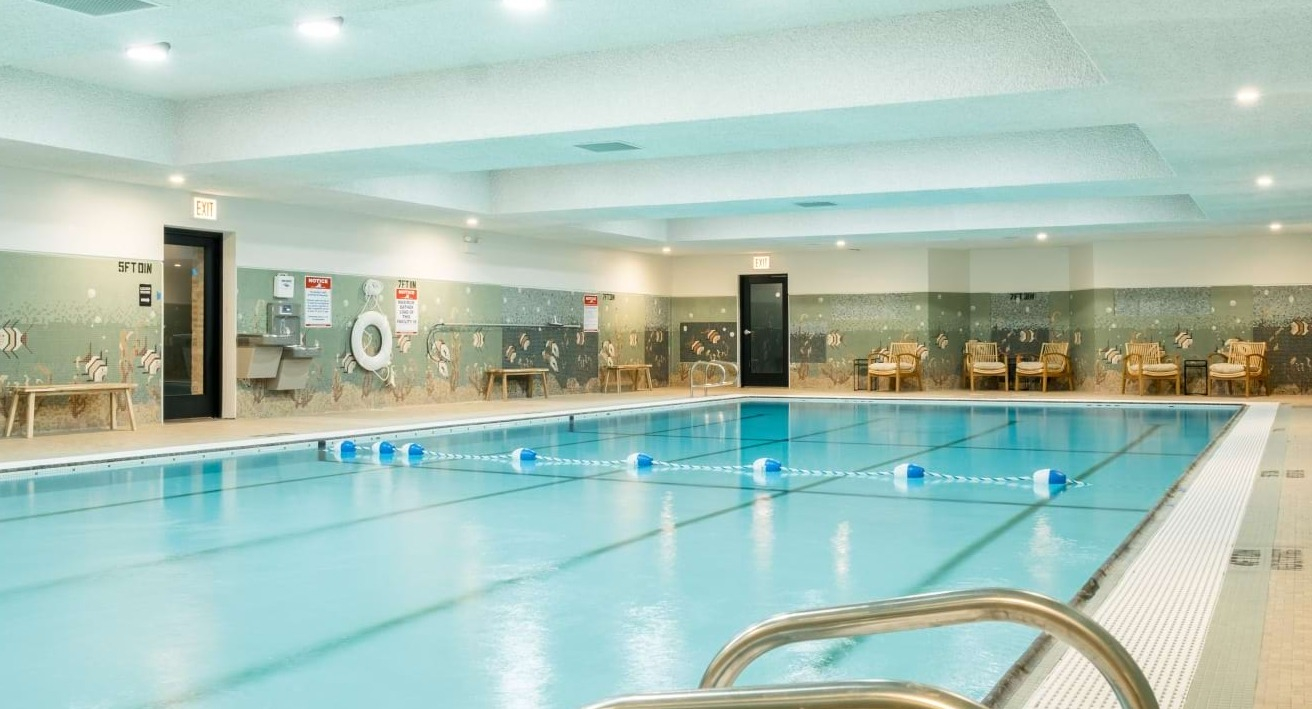 Spacious indoor swimming pool with decorative mosaic tiling, relaxation seating, and bright overhead lighting at The Duncan apartments in Chicago