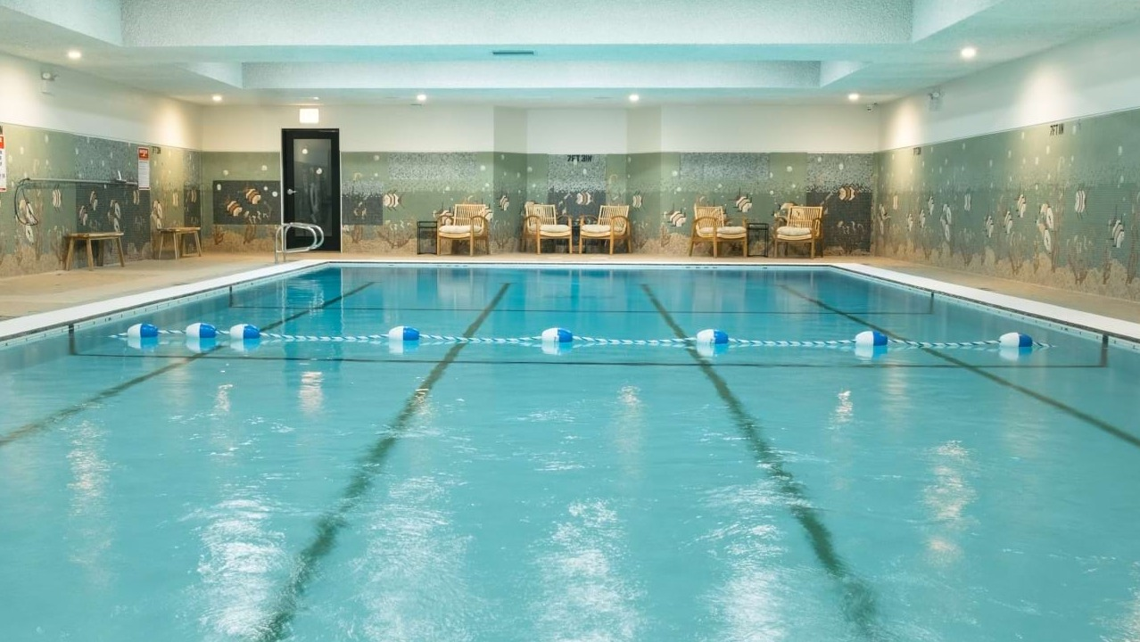 Inviting indoor swimming pool with lane markers, tiled walls, and comfortable lounge chairs, perfect for year-round swimming at The Duncan in Chicago