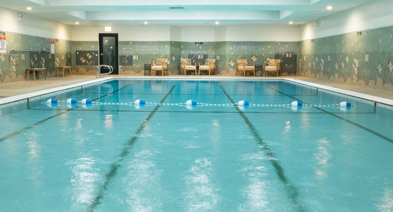 Inviting indoor swimming pool with lane markers, tiled walls, and comfortable lounge chairs, perfect for year-round swimming at The Duncan in Chicago