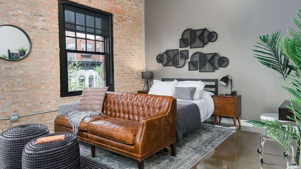 Chic loft-style bedroom with exposed brick, a comfortable bed, leather sofa, and modern decor at The Duncan apartments in Chicago