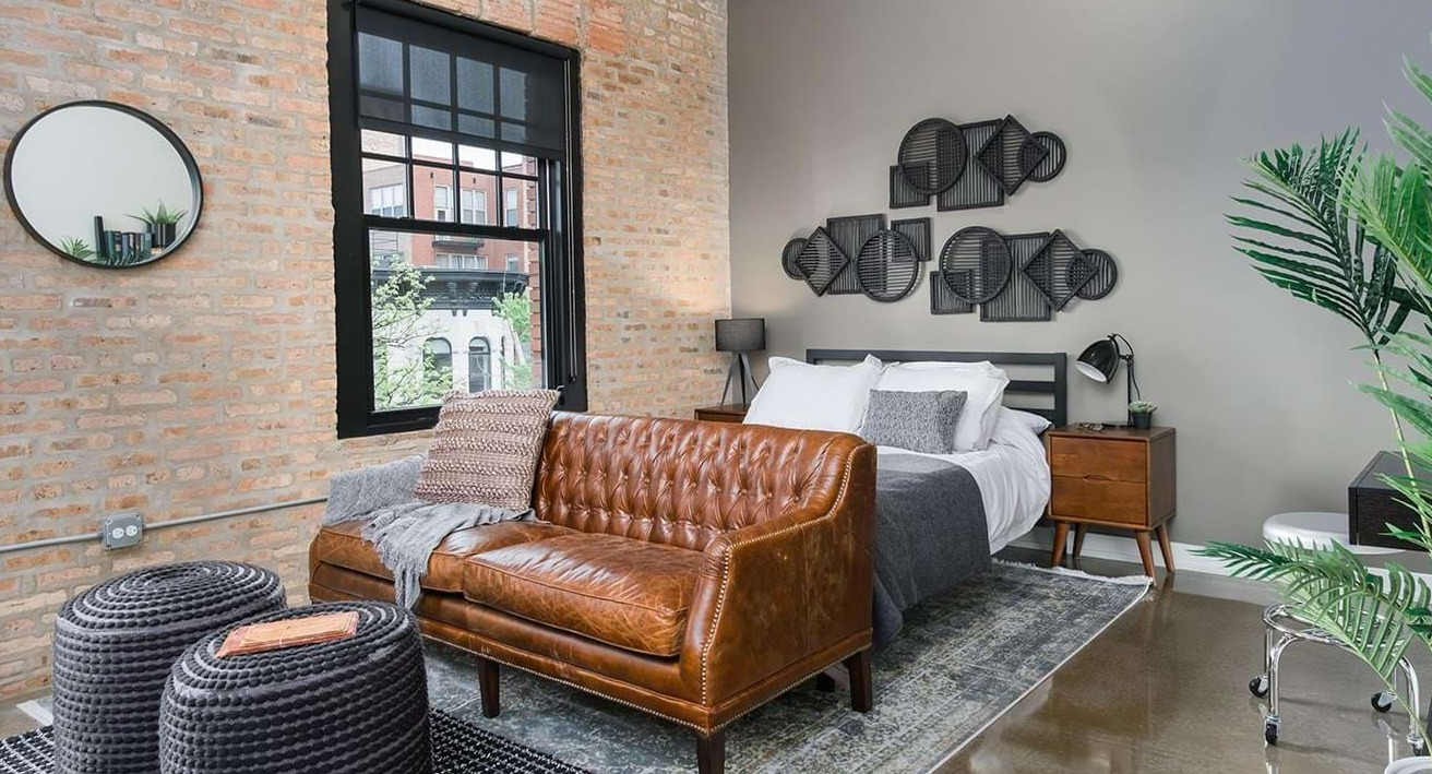 Chic loft-style bedroom with exposed brick, a comfortable bed, leather sofa, and modern decor at The Duncan apartments in Chicago
